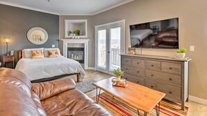 Un dormitorio moderno con cama, sofá de cuero, mesa de centro de madera, cómoda y televisor montado en la pared.