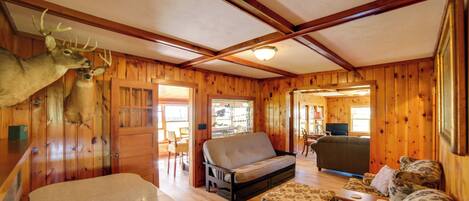 A wooden cabin interior with a sofa, ottoman, and a deer head mounted on the wall.