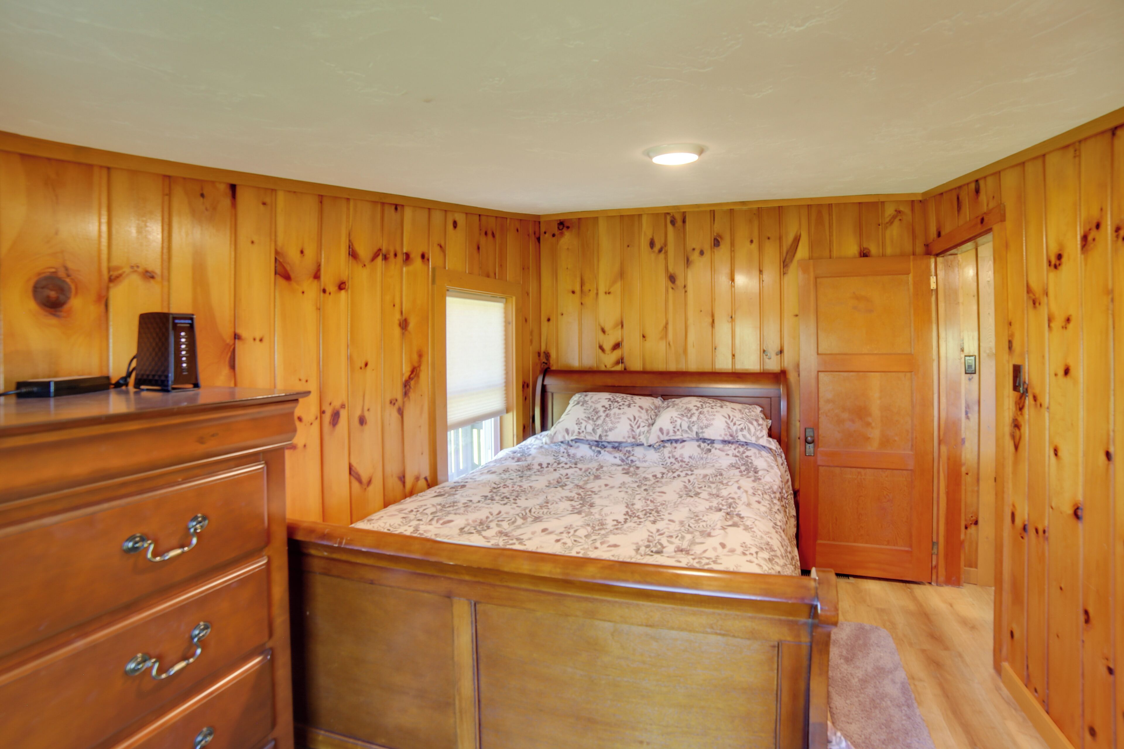 Un dormitorio con paneles de madera, una cama con colcha estampada, un aparador con cajones y una mesita de noche.