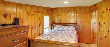 Un dormitorio con paneles de madera, una cama con colcha estampada, un aparador con cajones y una mesita de noche.