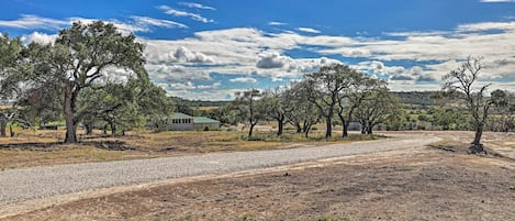 A rural landscape with a gravel road, trees, and a small building in the distance.