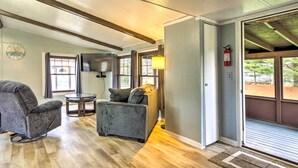 A room with a grey sofa, a smaller grey armchair, a round table, and a television mounted on the wall. - Cozy Sherrodsville Home: Walk to Lake Atwood! (Sherrodsville)