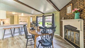 A dining area with a wooden table and black chairs, a kitchen in the background, and a fireplace with a vase of flowers. - Cozy Sherrodsville Home: Walk to Lake Atwood! (Sherrodsville)