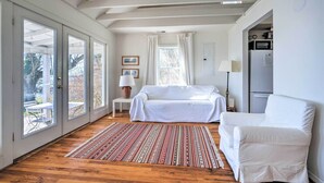 Una habitación amplia con una cama grande, un sillón blanco, una mesita con una lámpara y vistas a un espacio exterior a través de un ventanal.