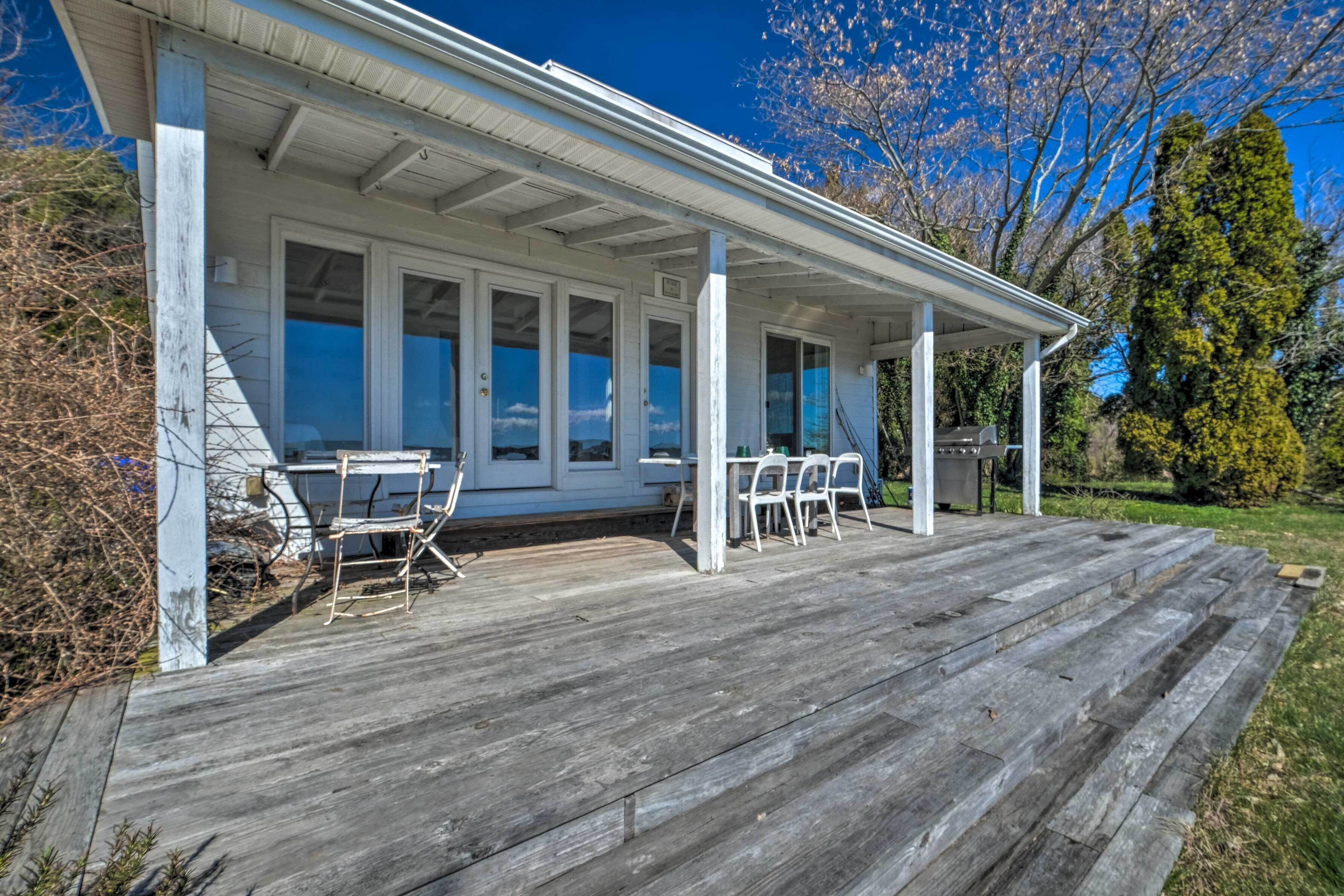 A covered porch with a wooden deck, white walls, and a windowed front.