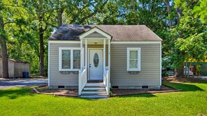A small, single-story house with a front porch and a door with a decorative glass panel. - Cozy Pantego Cottage ~ 5 Miles to Belhaven! (Pantego)