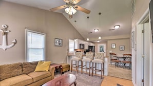 A living room with a brown sofa, a wooden coffee table, and a ceiling fan. There is a kitchen area with bar stools and a dining table with chairs. - Cozy Pantego Cottage ~ 5 Miles to Belhaven! (Pantego)
