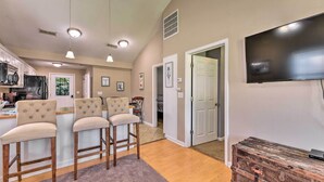 A kitchen with bar stools, a dining area, and a television mounted on the wall. - Cozy Pantego Cottage ~ 5 Miles to Belhaven! (Pantego)