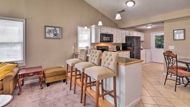 A kitchen with white cabinets, a microwave, and a refrigerator. There are three bar stools and a dining table with chairs. - Cozy Pantego Cottage ~ 5 Miles to Belhaven! (Pantego)