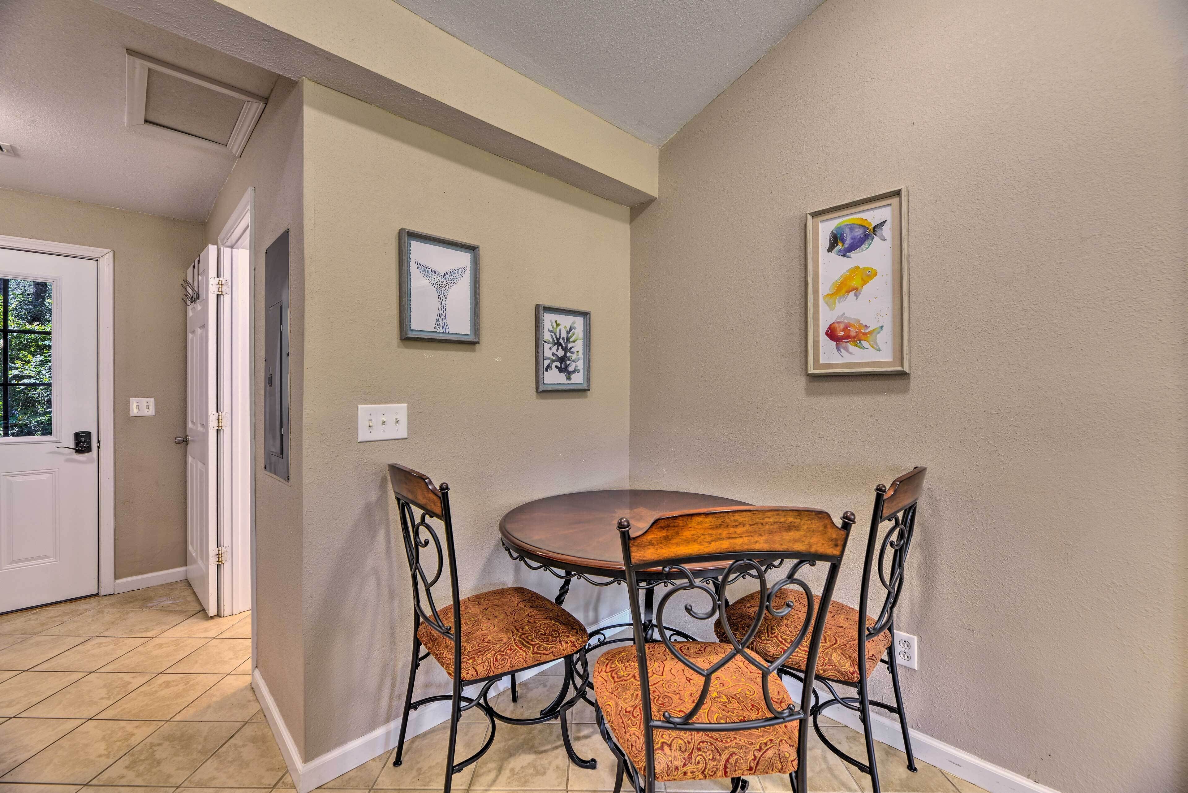 A dining area with a round table and four chairs, a door with a view, and two framed pictures on the wall.
