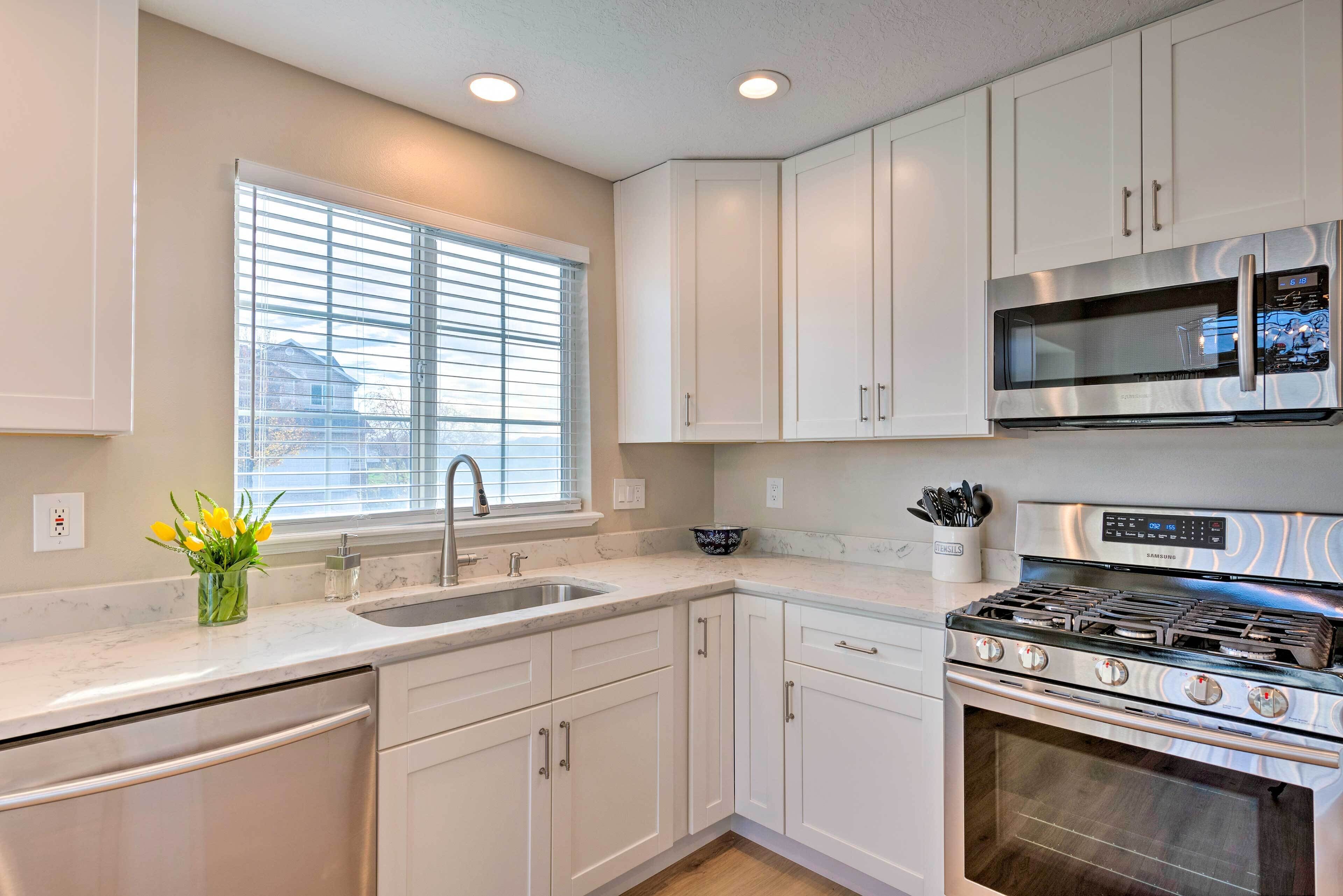 A modern kitchen with white cabinets, a stainless steel stove, a microwave, and a window with blinds.