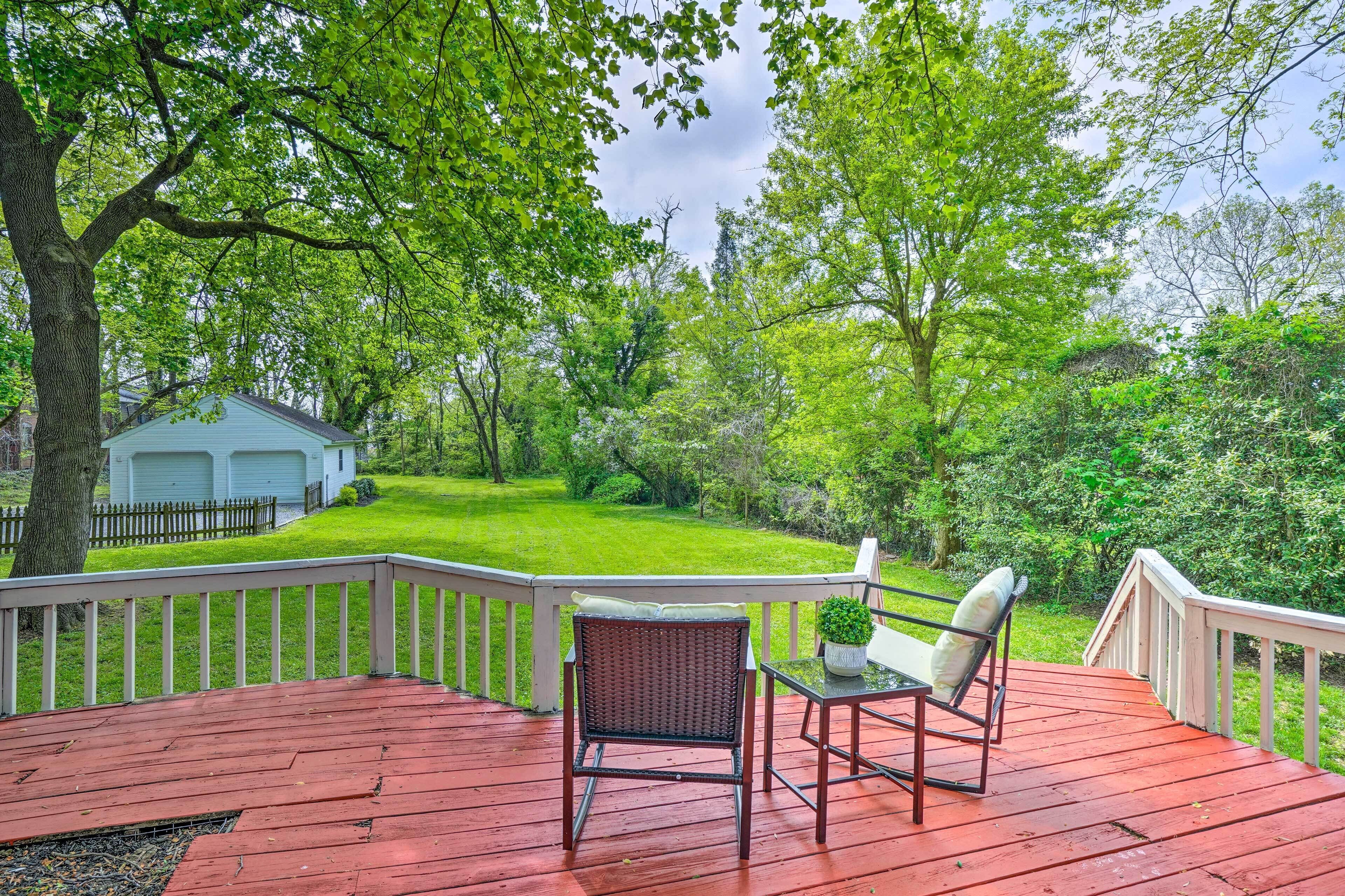 Une terrasse en bois avec deux chaises et une table, donnant sur une pelouse verdoyante et un garage blanc.