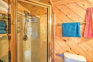 A wooden-paneled bathroom with a glass shower enclosure, a toilet, and towels hanging on a rack. - Dreamy Bucksport Hideaway on Freshwater Pond! (Bucksport)