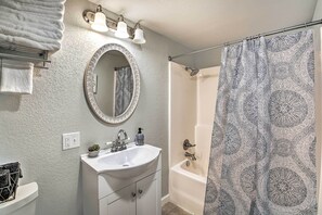 A bathroom with a white sink, mirror, and toilet. There is a shower curtain with a patterned design.
