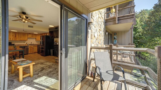 A modern kitchen with wooden cabinets, a dining area with a table and chairs, and a sliding glass door leading to a balcony with a stone wall and a wooden deck. - Cozy Sevierville Condo: Balcony, Pool Access (Sevierville)