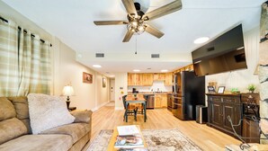 A modern living room with a sofa, a coffee table with magazines, a ceiling fan, and a kitchen area with wooden cabinets and appliances. - Cozy Sevierville Condo: Balcony, Pool Access (Sevierville)