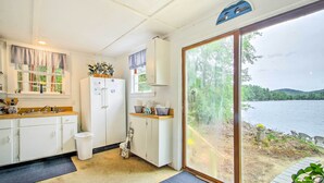 Una cocina con armarios blancos, un refrigerador y una ventana con vistas a un lago.