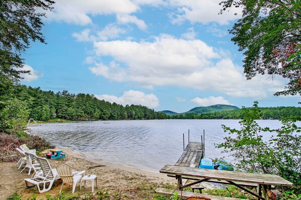Un entorno junto al lago con un muelle de madera, sillas de playa y una mesa de picnic.