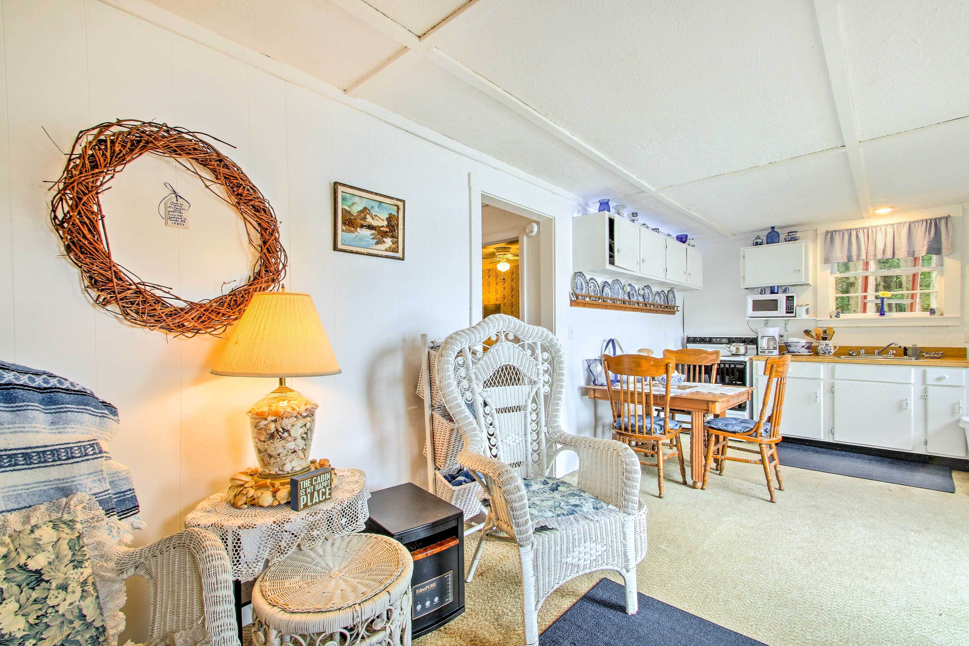 Een gezellige woonkamer met rieten meubels, een eethoek en een keuken met witte kastjes en een raam.