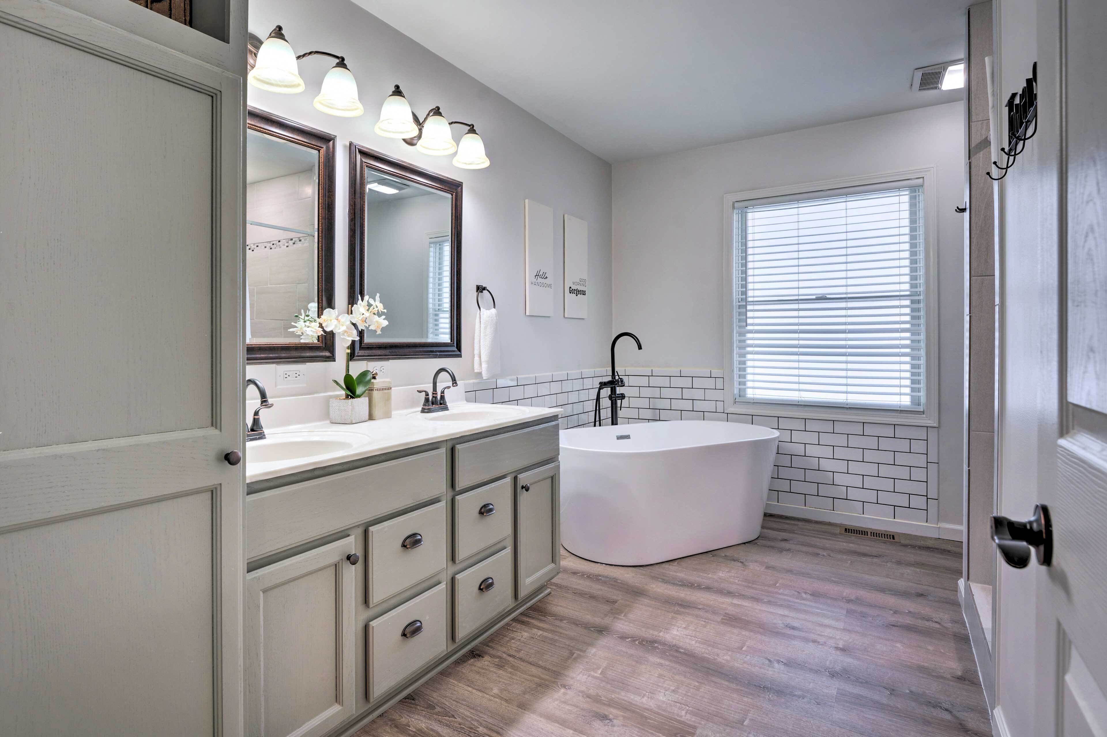 A bathroom with a vanity, a large mirror, a bathtub, and a window with blinds.