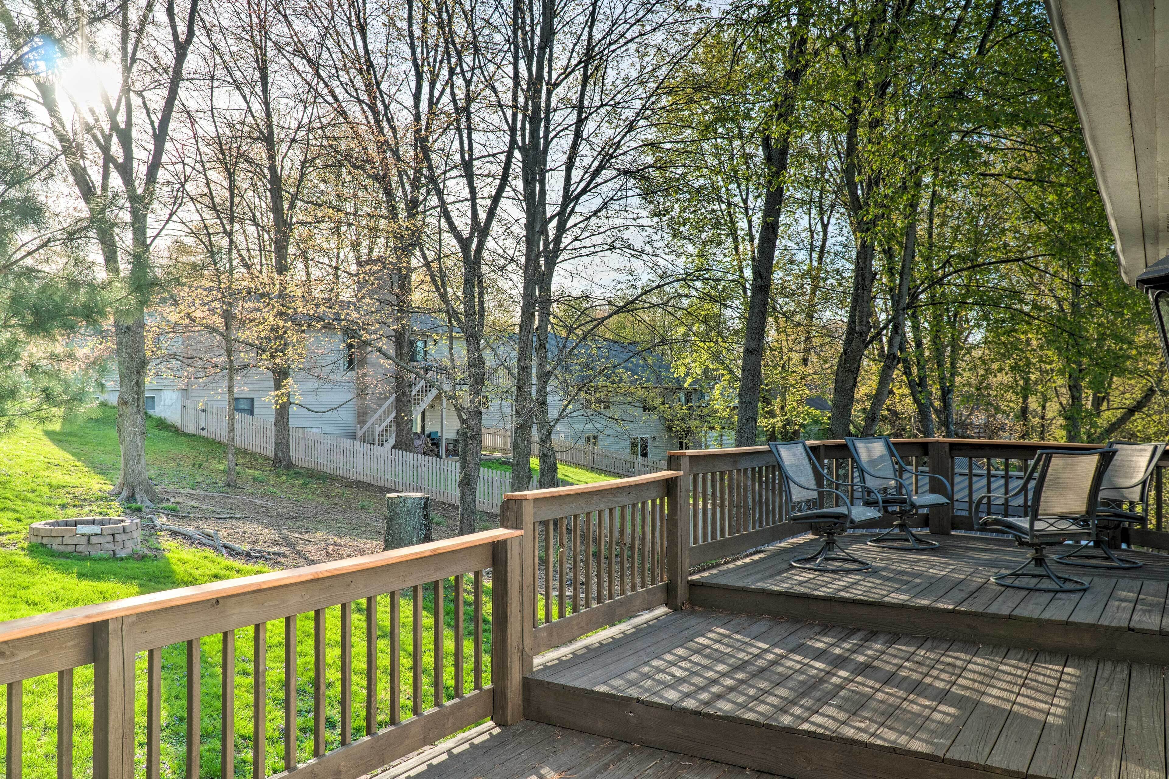 A wooden deck with outdoor furniture, surrounded by trees and a grassy yard.