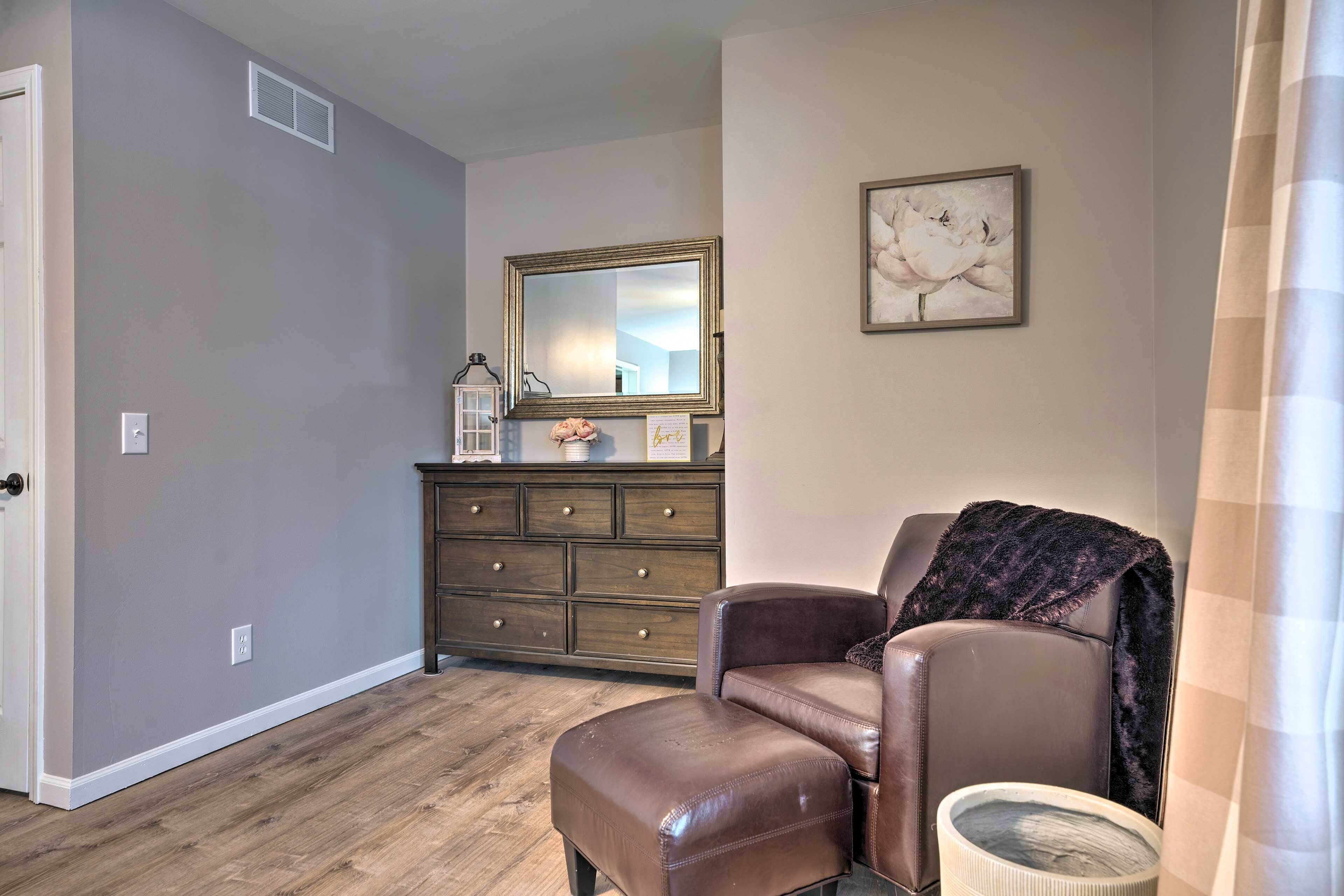 A room with a brown leather chair, a wooden dresser, a mirror, and a framed picture on the wall.