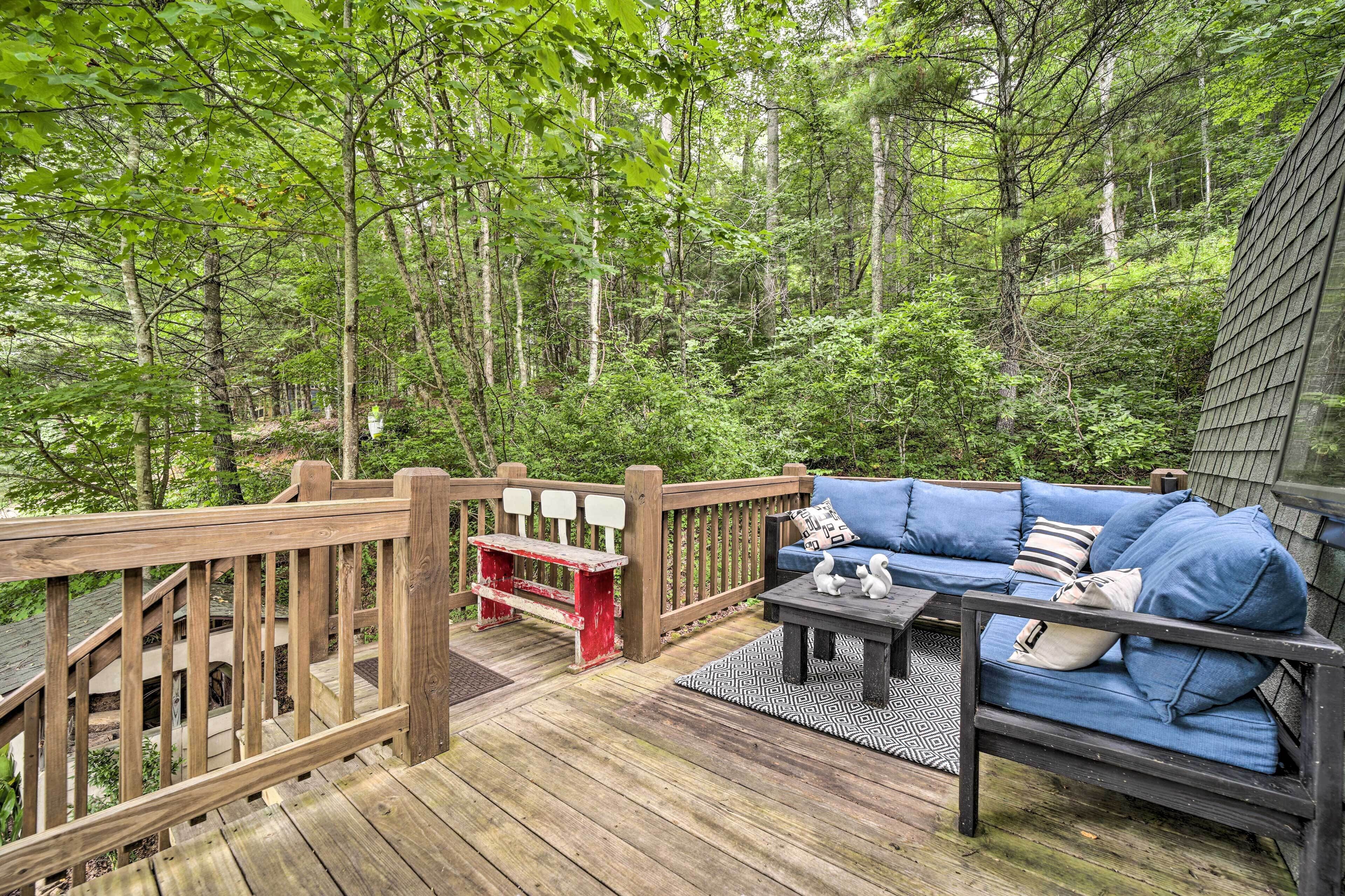 Eine Holzterrasse mit einem blauen Sofa und einem kleinen Tisch, umgeben von einem Wald.