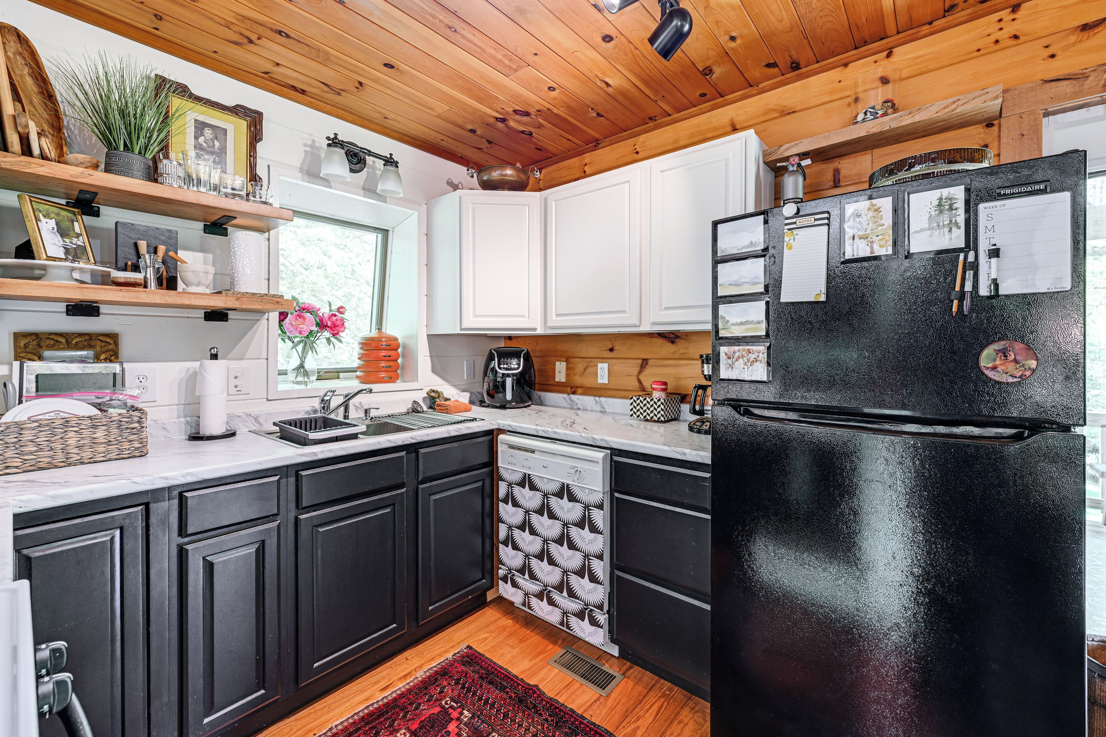 A kitchen with black cabinets, a black refrigerator, a dishwasher, and wooden shelves with various items.