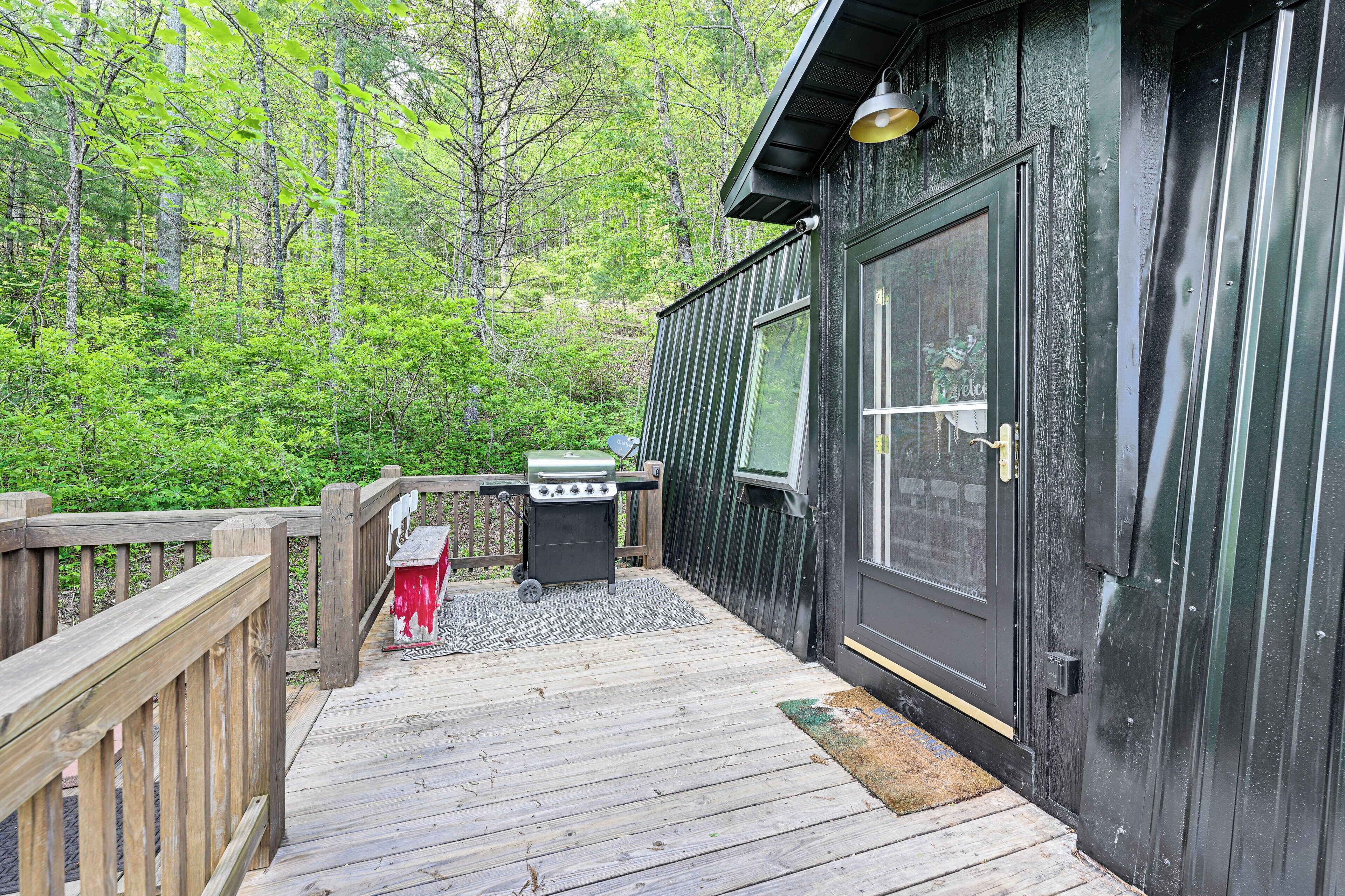 A wooden deck with a grill and a door to a cabin.