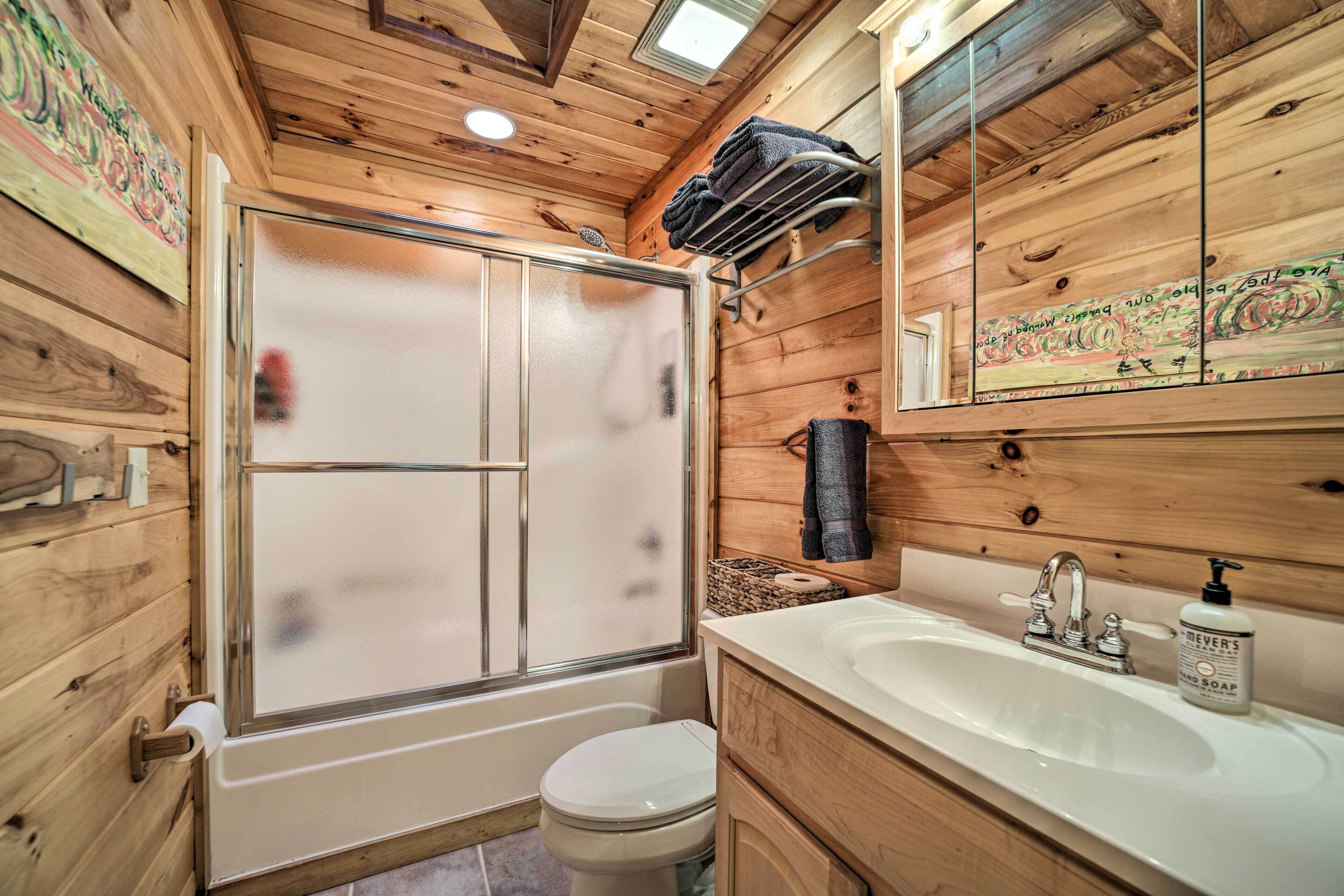 Een houten badkamer in een vakantiehuisje, met douche, toilet, wastafel en spiegel.