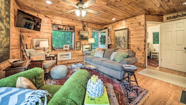 A cozy cabin interior with wooden walls, a gray sofa, a green armchair, and a ceiling fan.