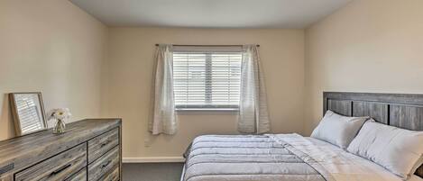 Ein Schlafzimmer mit einem Bett, einer Kommode, einem Fenster mit Vorhängen und einer Deckenleuchte.