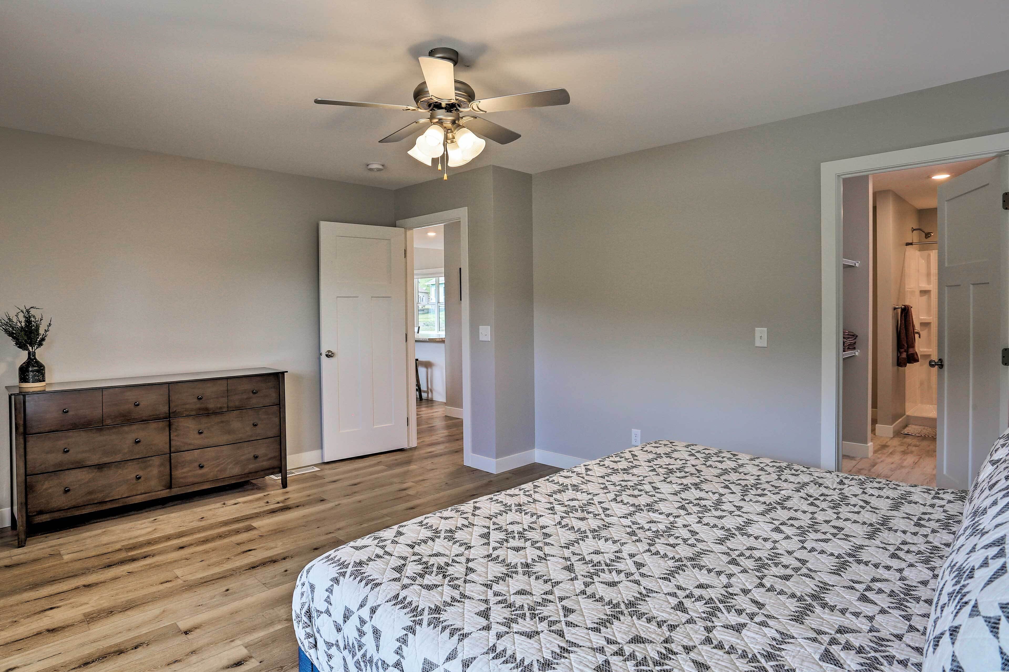 A bedroom with a bed, a dresser, a ceiling fan, and a door leading to another room.