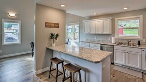 A modern kitchen with white cabinets, granite countertops, and a central island with stools. - Heart of Black Hills Home by Mickelson Trail! (Hill City)