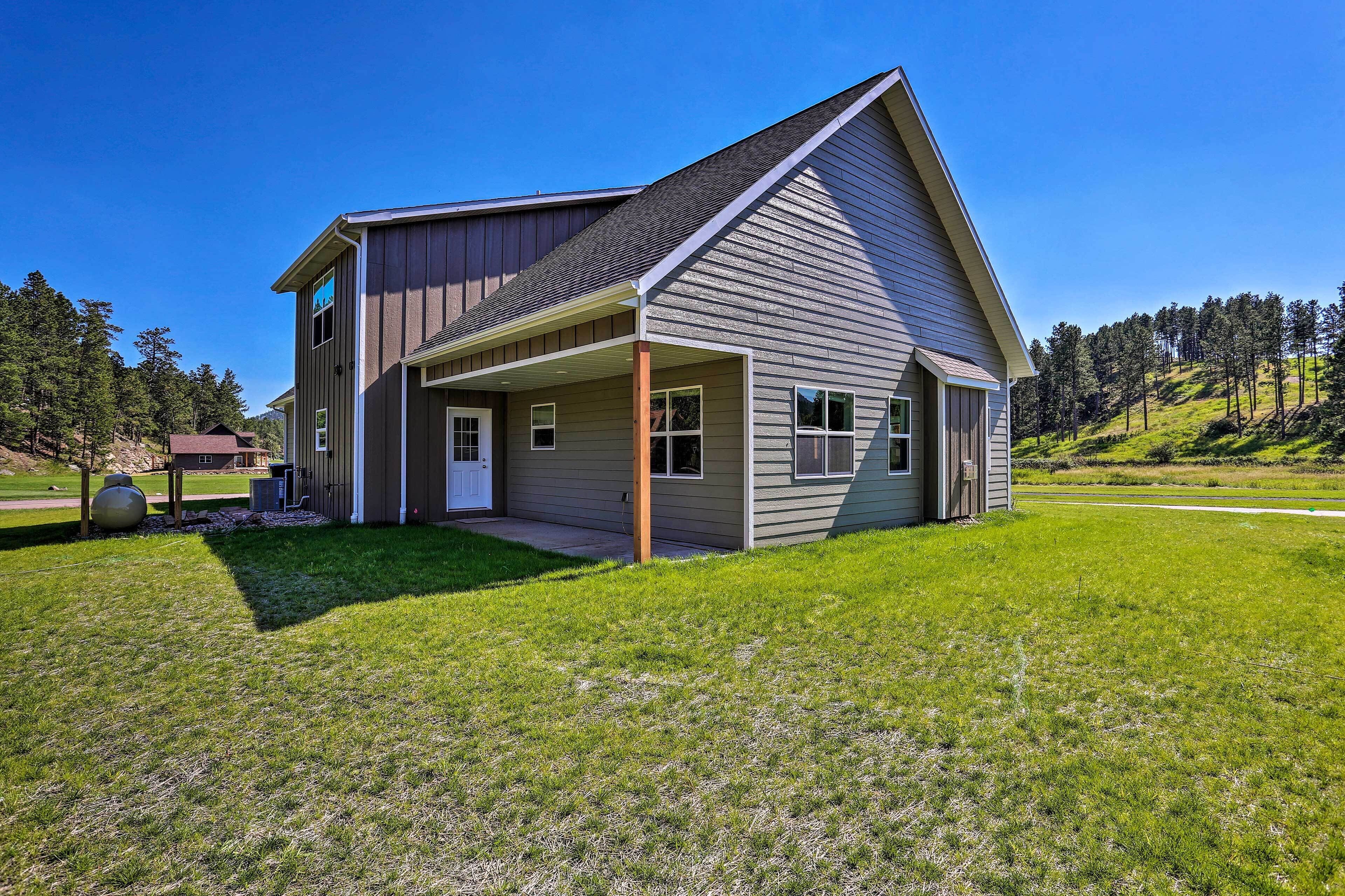 A modern two-story house with a covered porch, surrounded by a well-maintained lawn and a forested hillside.