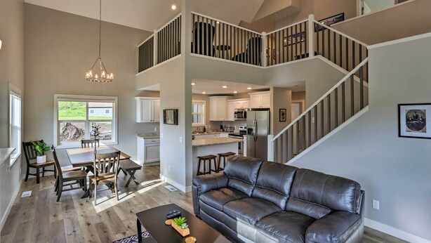 A spacious living area with a leather sofa, dining table, and chairs, a staircase leading to a loft, and a kitchen in the background. - Heart of Black Hills Home by Mickelson Trail! (Hill City)
