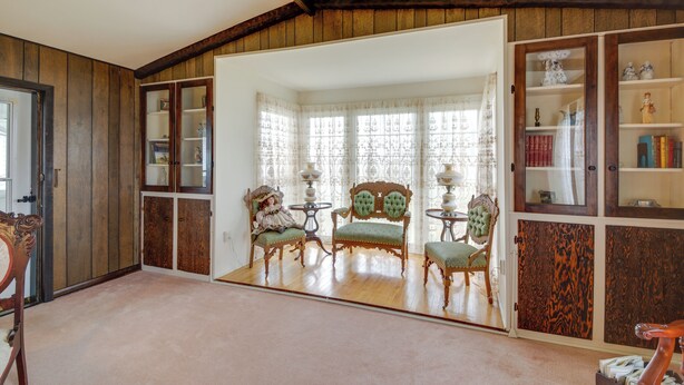 A room with wooden paneling, a large mirror, two green upholstered chairs, a small table, and a bookshelf with decorative items. - Historic Alexandria Home w/ Private Yard! (Alexandria)