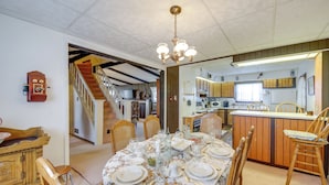 A dining area with a table set for four, wooden chairs, a chandelier, and a kitchen in the background. - Historic Alexandria Home w/ Private Yard! (Alexandria)