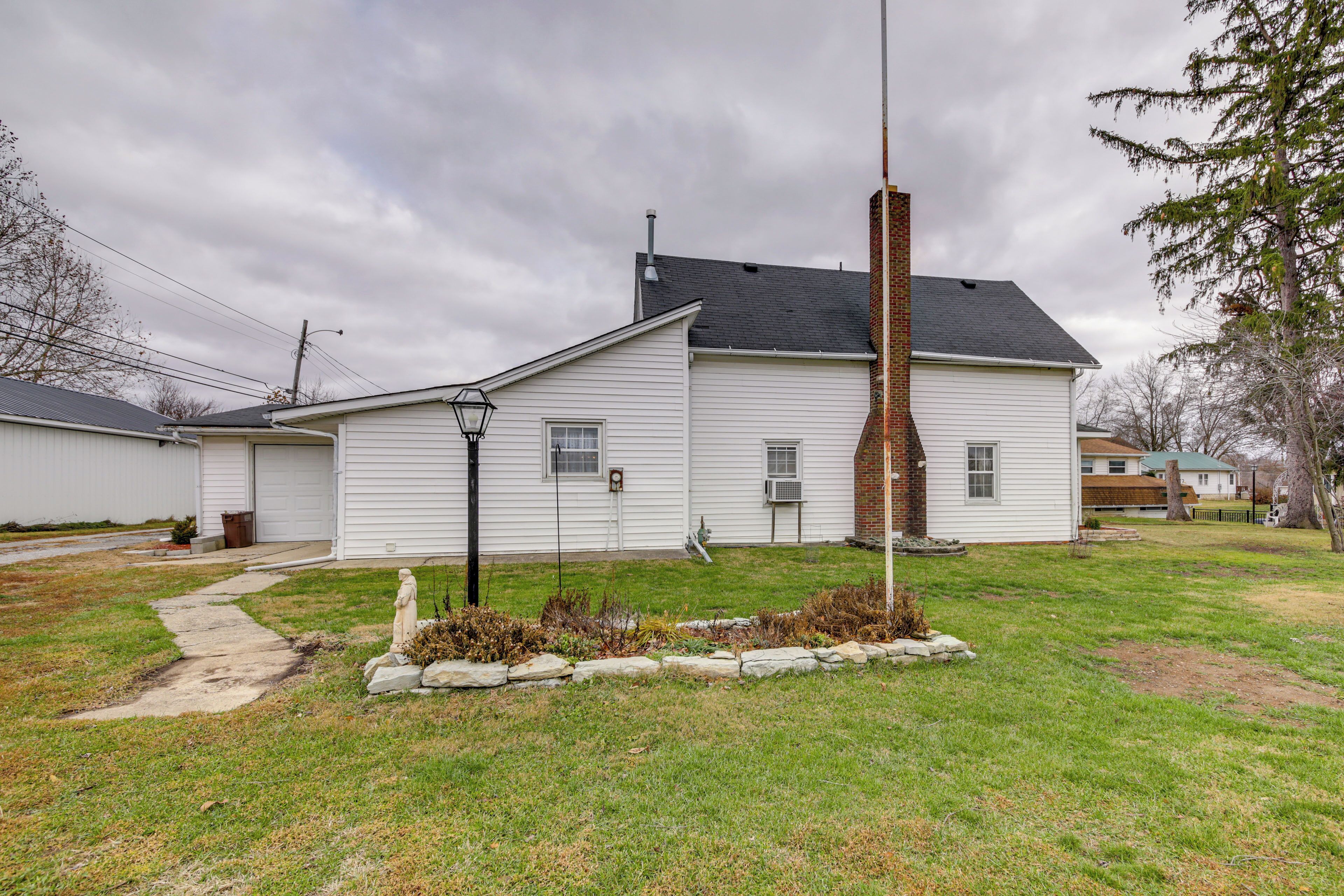 A single-story house with a brick chimney, a front yard with a stone border, and a sidewalk leading to the garage.