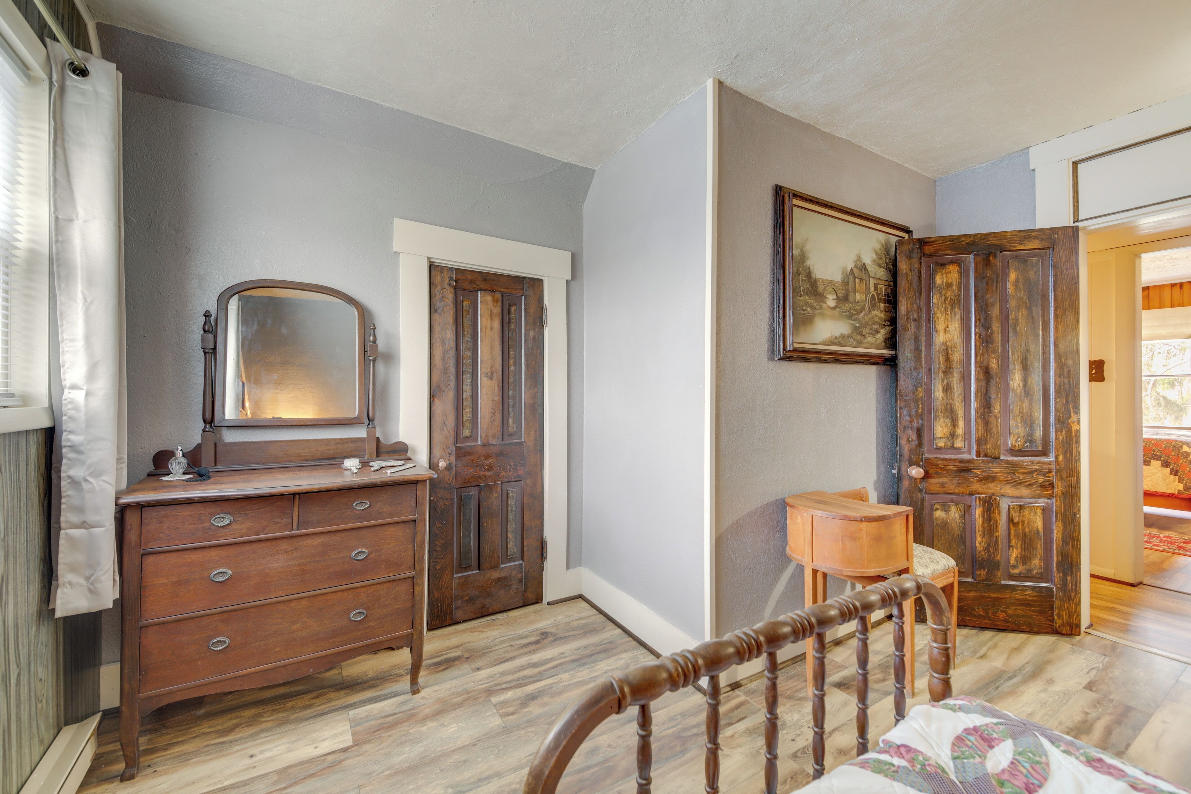 Un dormitorio con un aparador de madera, una silla, una cama y una puerta que da a otra habitación.