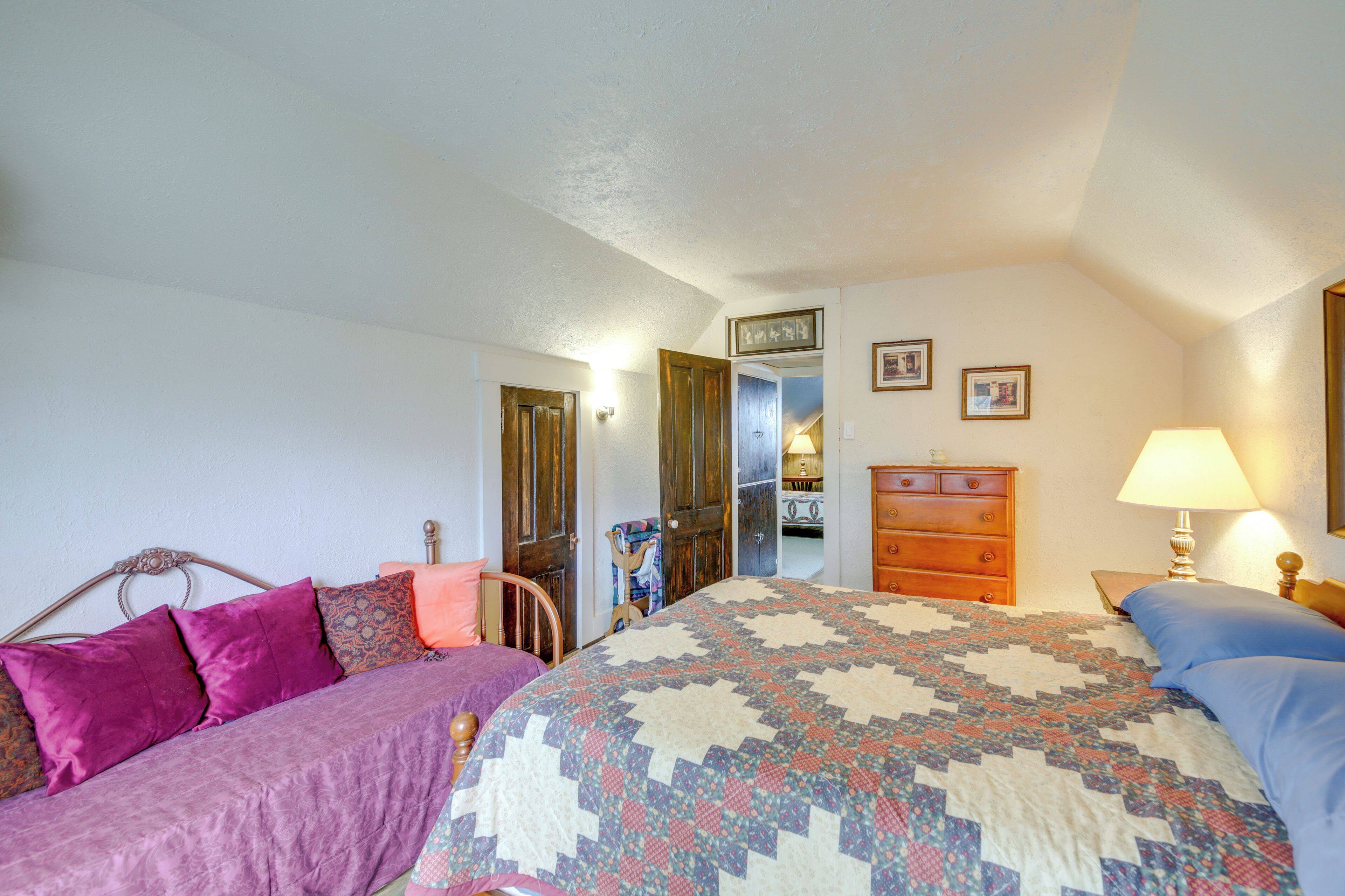 A bedroom with a bed, dresser, nightstand, and a door leading to another room.
