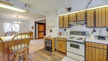 A kitchen with wooden cabinets, a stove, and a small oven. There is a wooden chair and a dining table in the background.