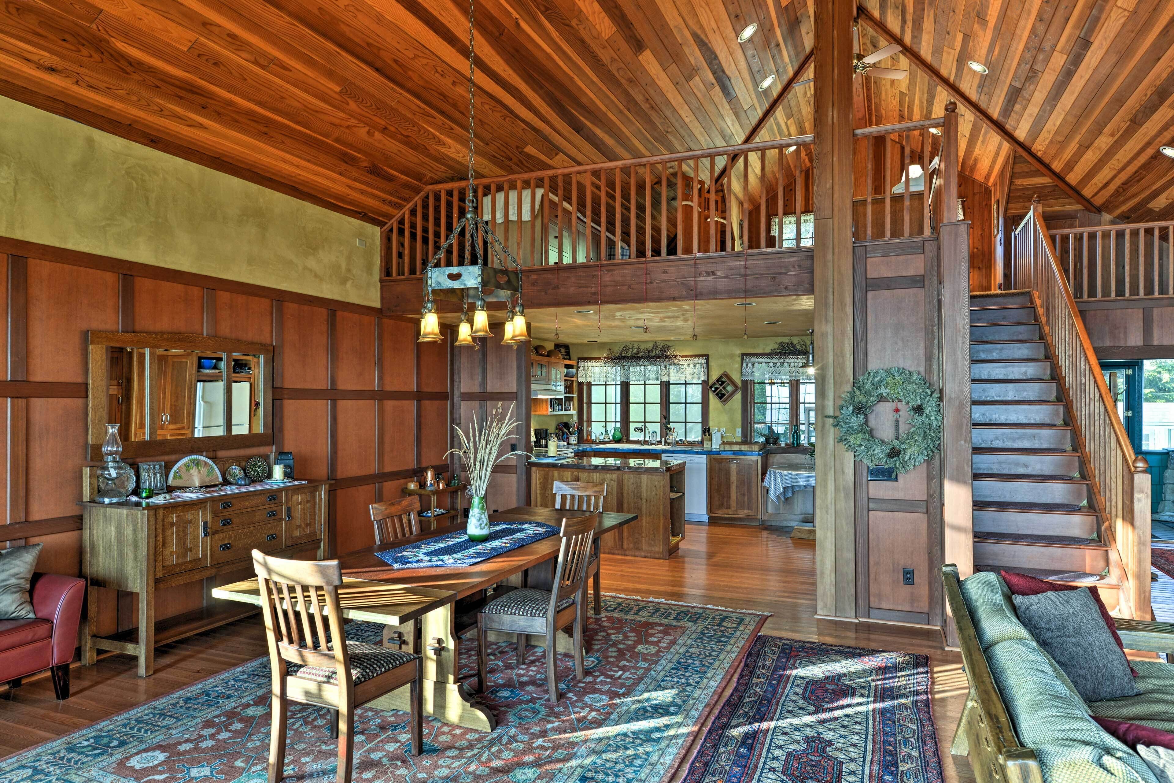 A spacious living area with a wooden ceiling, a dining table with chairs, a sofa, and a staircase leading to an upper level.