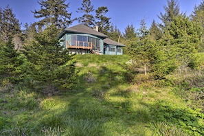 A house with a curved roof and large windows, surrounded by dense forest and grass. - Forested Gold Beach House w/ Panoramic Ocean Views (Gold Beach)