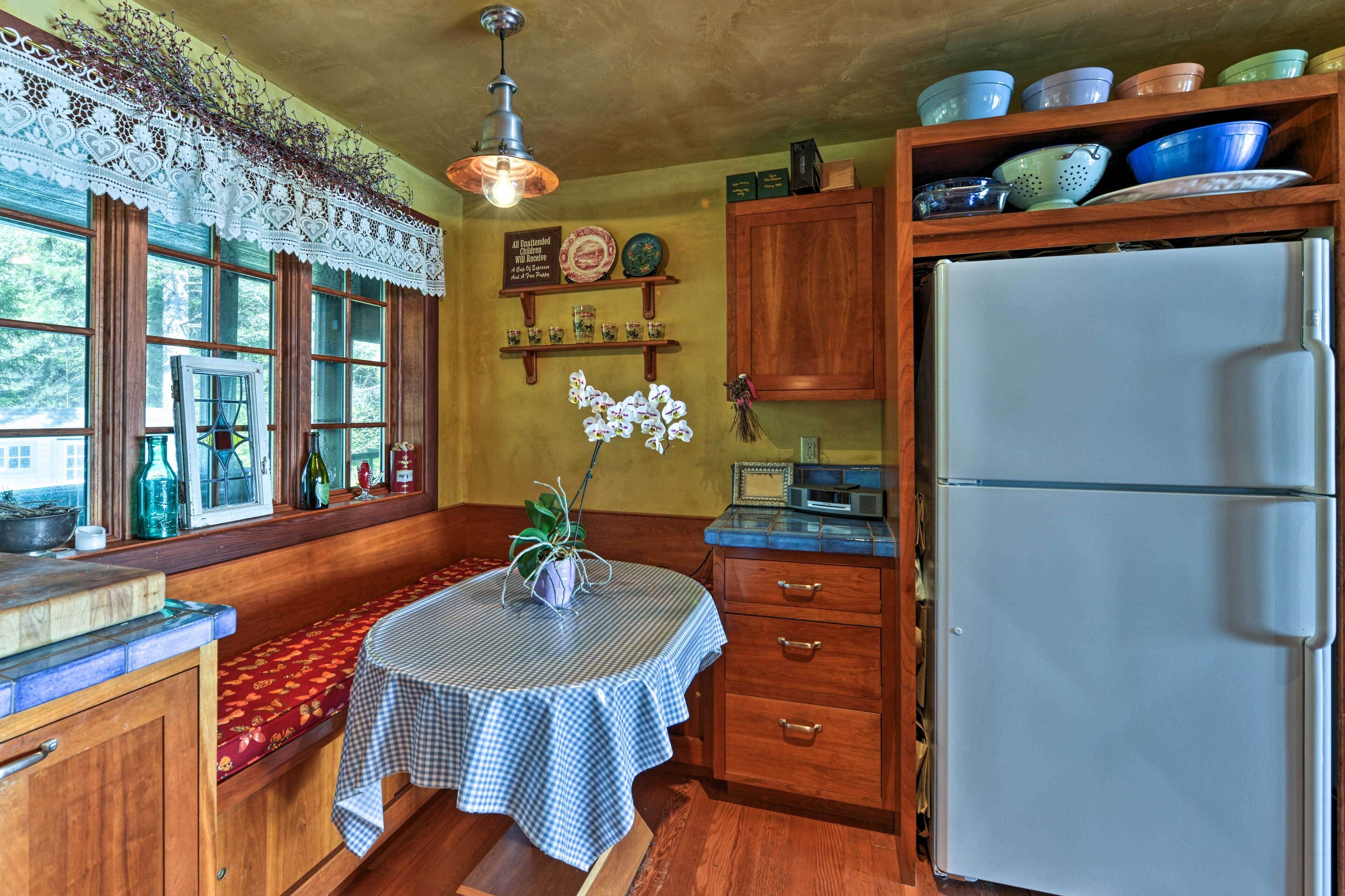 A kitchen with wooden cabinets, a refrigerator, a window with a view, and a table with a checkered tablecloth.