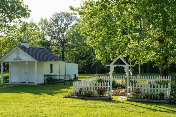 A small white building with a porch and a fenced garden area with flowers.