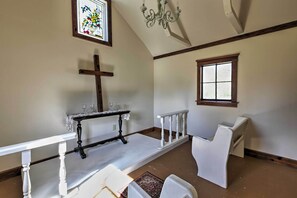 A chapel with a white altar, pews, a stained glass window, and a wooden ceiling.