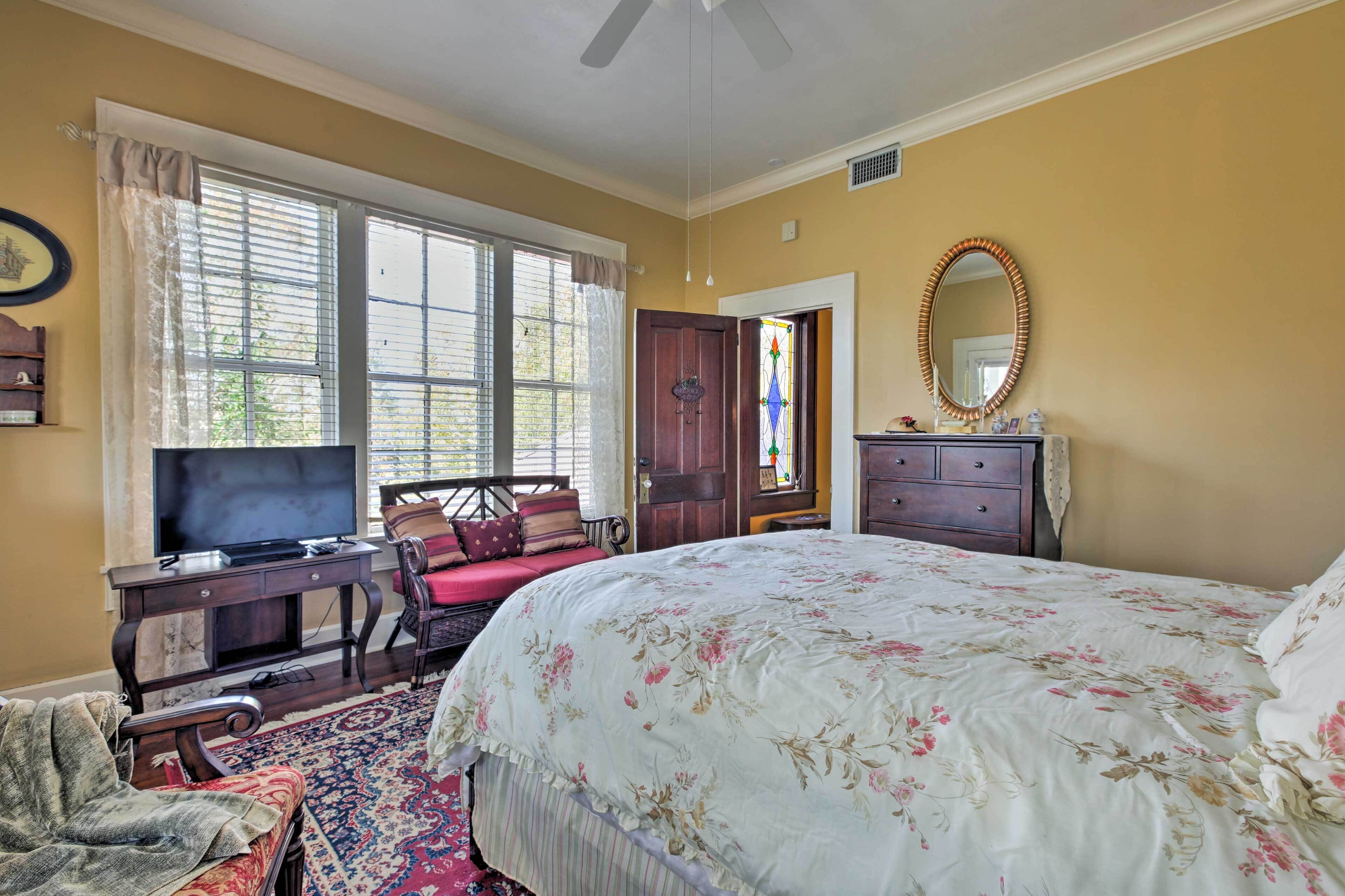 A bedroom with a large bed, a desk with a television, a chair, a dresser, and a window with curtains.