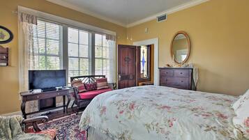 A bedroom with a large bed, a desk with a television, a chair, a dresser, and a window with curtains.