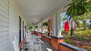 A covered porch with white rocking chairs, a brick wall, and hanging plants. - Historic Huntington Home w/ Pond & Flower Gardens! (Huntington)